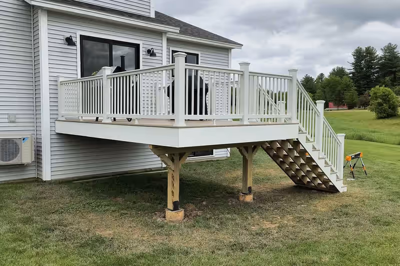Raised attached deck with white vinyl railing and tan composite decking on a Vermont home, built by Empirical Renovations
