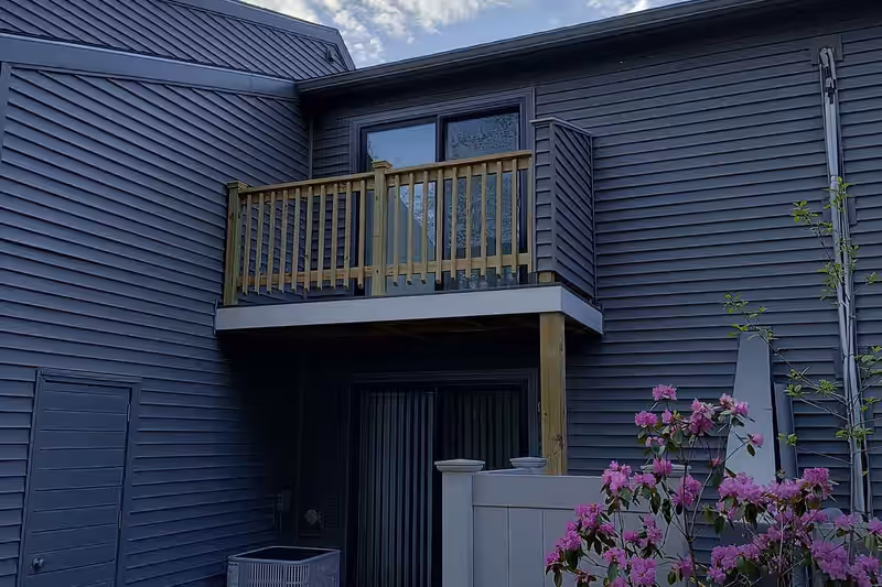 Second-storey balcony deck with new pressure-treated railing cantilevered above a doorway on a Vermont home, built by Empirical Renovations