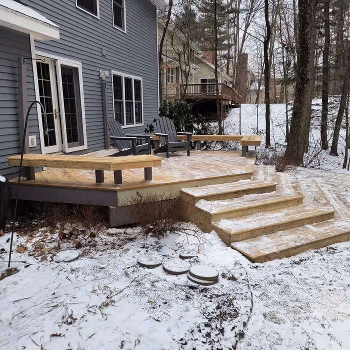 Bare pressure-treated deck with built-in benches and wraparound steps before staining at a Vermont home, snow on the ground