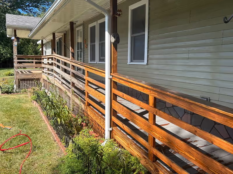 Porch railing half pressure washed by Empirical Renovations, clean bright wood on one side and weathered gray on the other