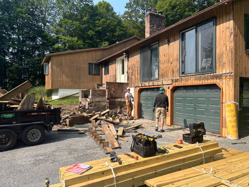 Empirical Renovations crew tearing out an old deck and brick landing with debris loaded into a dump trailer in Vermont