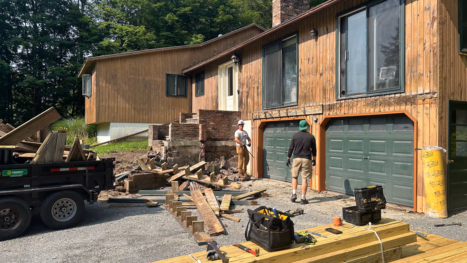 Empirical Renovations crew tearing out an old deck and brick landing with debris loaded into a dump trailer in Vermont
