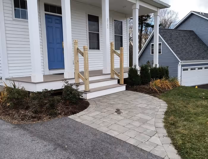 New pressure-treated stair railings on a white front entry porch with a blue door, built by Empirical Renovations in Vermont