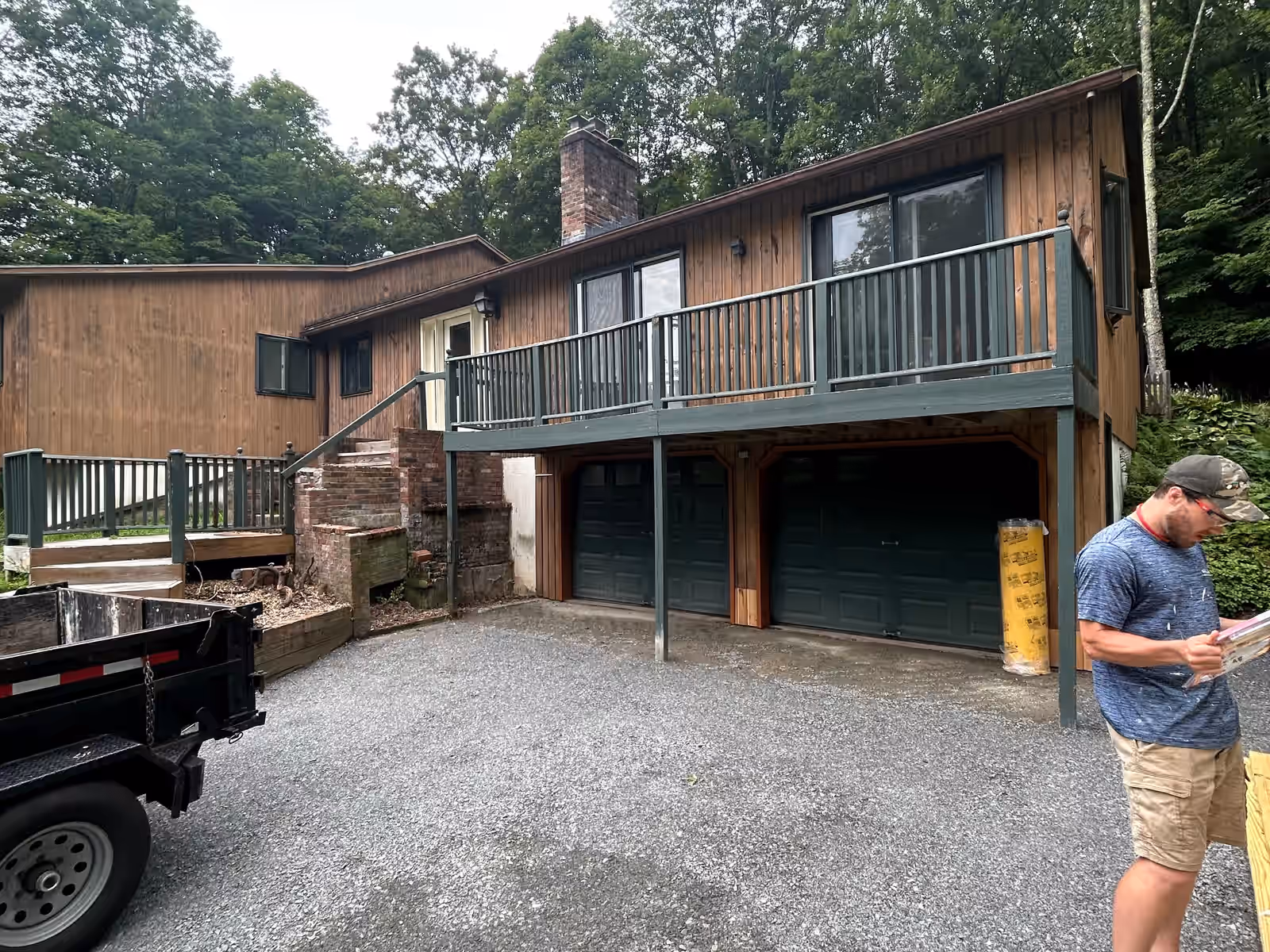 Elevated deck with green railings spanning the front of a Vermont home above the garage, before demolition by Empirical Renovations