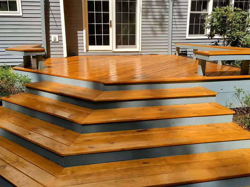 Deck and wraparound steps finished in a warm amber stain with painted grey risers by Empirical Renovations in Vermont