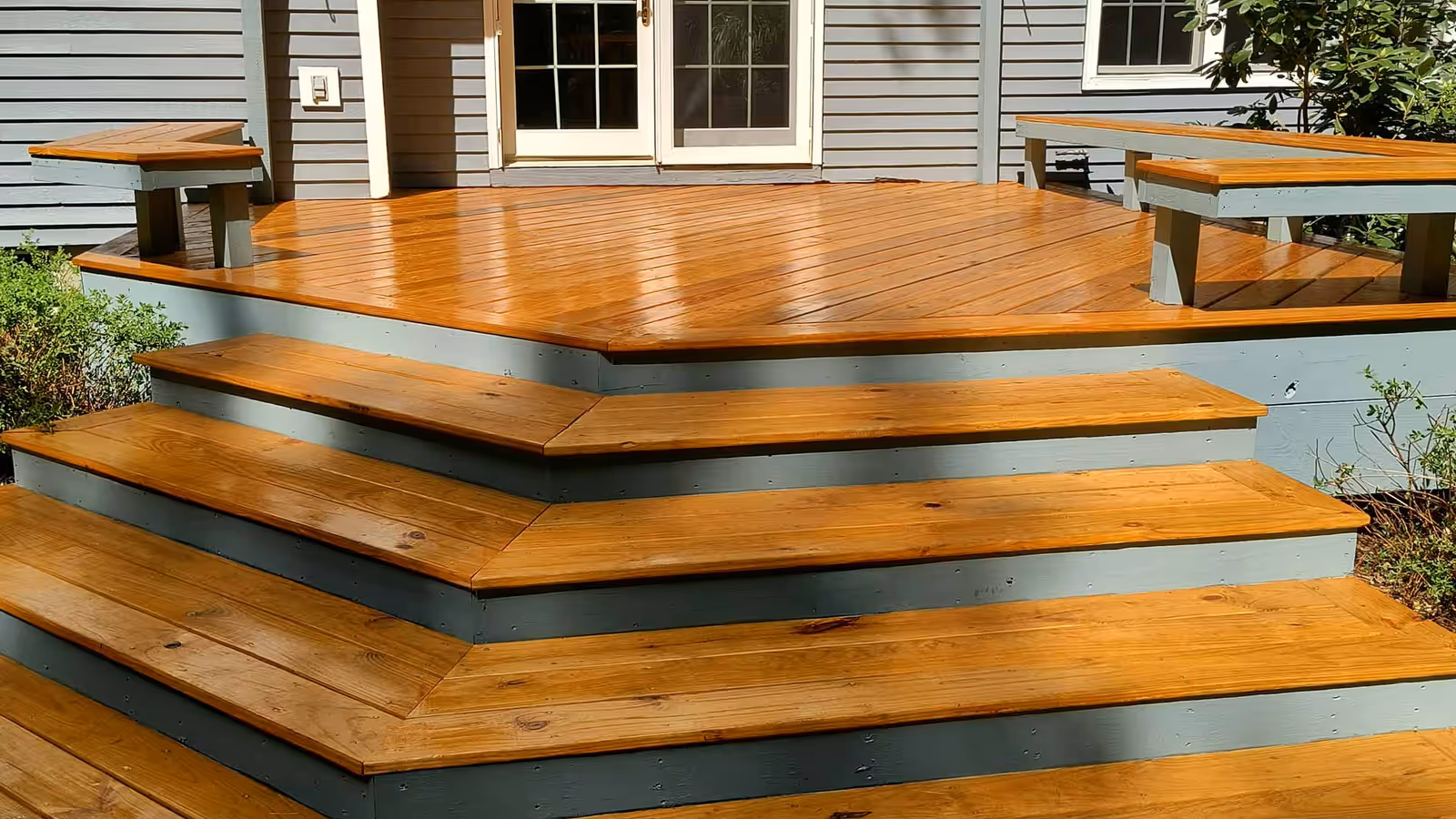Deck and wraparound steps finished in a warm amber stain with painted grey risers by Empirical Renovations in Vermont