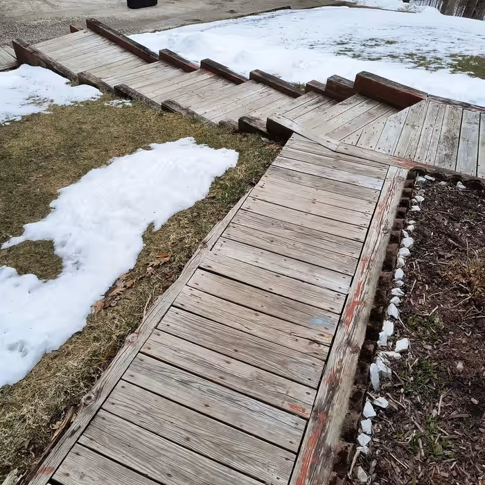 Weathered wooden walkway and steps with greyed boards and traces of old red stain, snow on the ground, before rebuilding at a Vermont home