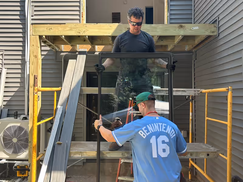 Empirical Renovations crew lifting a glass patio door into a second-storey opening above new deck framing in Vermont