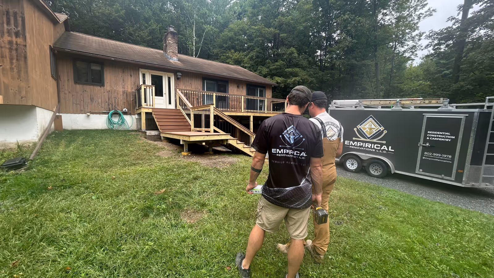Empirical Renovations crew walking up to a newly built deck and stairs at a Vermont home, with the company work trailer parked alongside