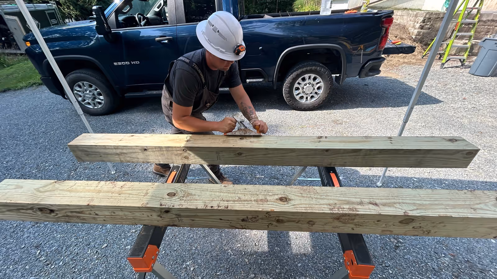 Empirical Renovations carpenter marking out pressure-treated beams on sawhorses at a Vermont job site