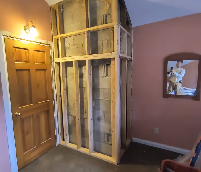 Stud wall framing built out around an exposed block chimney chase in a Vermont bedroom by Empirical Renovations
