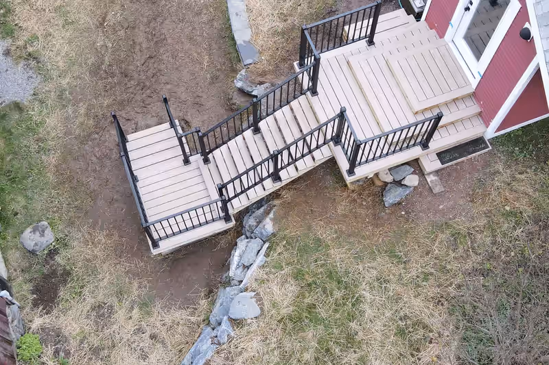 Aerial view of a front entry deck with tan composite decking and black aluminium railing at a red Vermont home, built by Empirical Renovations