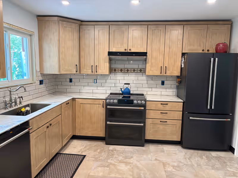 Kitchen remodel with a white tile backsplash, blue marble countertops, new wood cabinets and new appliances, completed by Empirical Renovations in Vermont