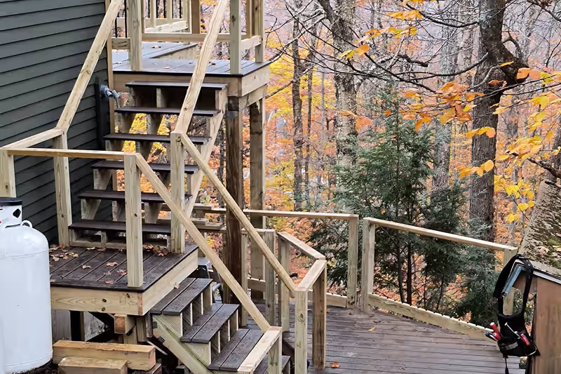 Multilevel deck with new pressure-treated stairs stepping down a wooded Vermont hillside, built by Empirical Renovations