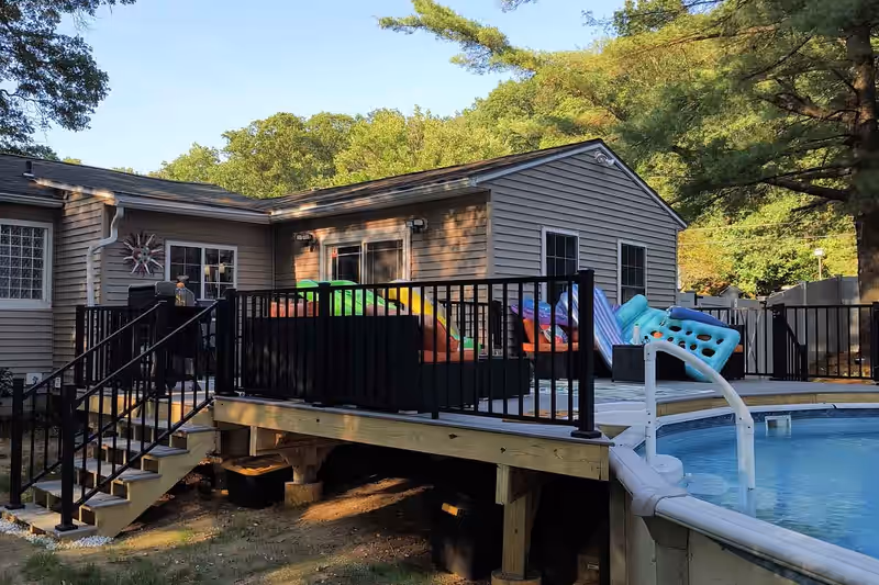 Deck built alongside an above-ground pool with black aluminium railing on a Vermont property, by Empirical Renovations